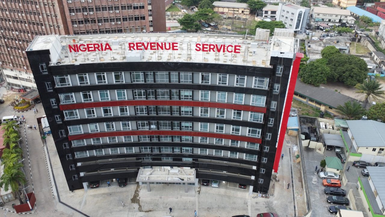 Aerial photograph of the completed Nigeria Revenue Service headquarters building in Ikoyi, Lagos, showing its curved black facade with red accent bands.